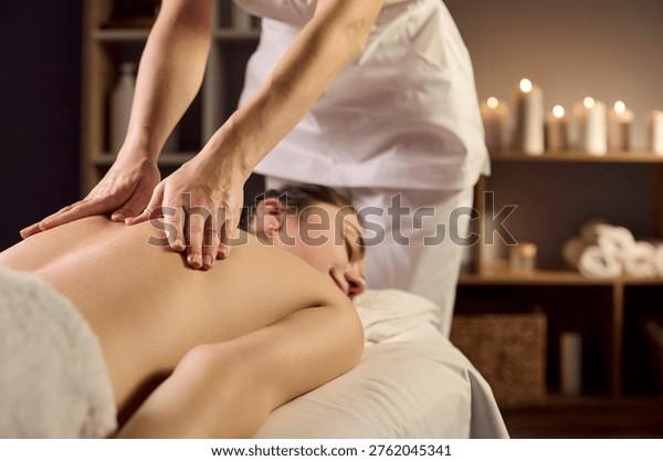 Bàn tay của kỹ thuật viên nữ đang nhẹ nhàng đặt những viên đá nóng dọc cột sống lưng khách hàng, không gian trị liệu ấm cúng với ánh nến và tinh dầu