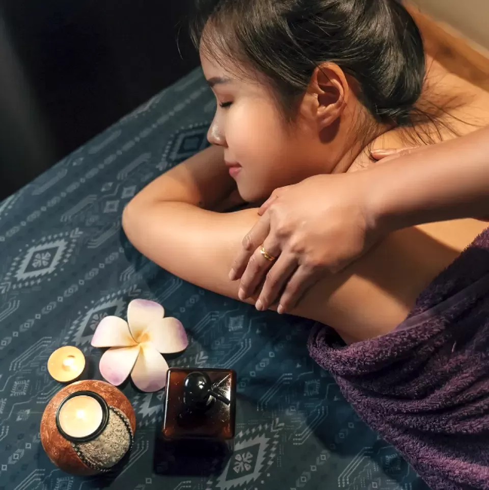 Người phụ nữ một mình trong phòng massage ấm cúng, nến thơm và tinh dầu, ánh mắt nhắm nhẹ thư giãn sâu