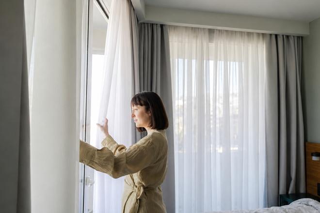 Người phụ nữ du lịch một mình đang nằm thư giãn trên giường khách sạn, kỹ thuật viên nhẹ nhàng massage lưng, rèm cửa kéo kín, không gian yên tĩnh và an toàn tuyệt đối