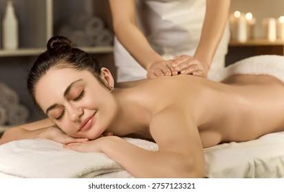 Một người phụ nữ đang nằm thư giãn trên bàn massage, kỹ thuật viên đang thực hiện các động tác massage nhẹ nhàng vùng bụng dưới, không gian phòng tối với nến thơm và tinh dầu
