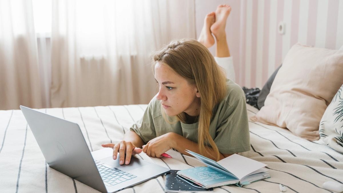Hình ảnh người phụ nữ trẻ ngồi bên máy tính làm việc muộn trong phòng ngủ, biểu cảm mệt mỏi, xung quanh là gối ôm và chăn ấm, không gian yên tĩnh