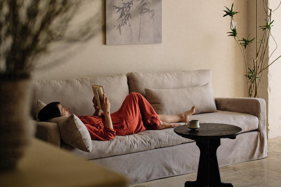 Một phụ nữ đơn thân thư giãn đọc sách và uống trà trong không gian ấm cúng sau buổi massage yoni, cảm giác tự do và an nhiên