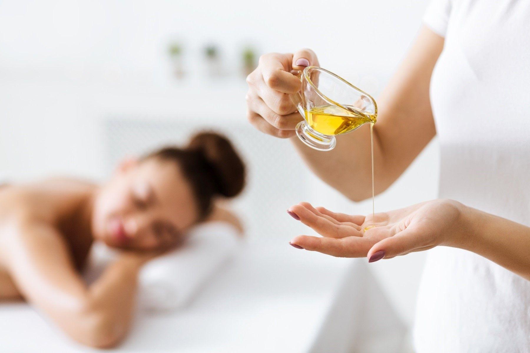 Bàn tay chuyên nghiệp của therapist đang thoa tinh dầu nhẹ nhàng lên lưng khách hàng, thể hiện sự tinh tế