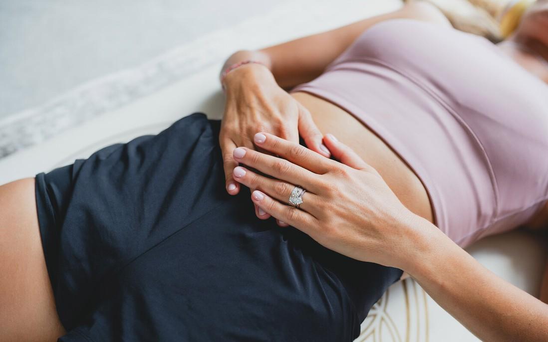 Bàn tay chuyên viên massage nhẹ nhàng vùng bụng dưới và khung xương chậu, tạo cảm giác an toàn và chuyên nghiệp