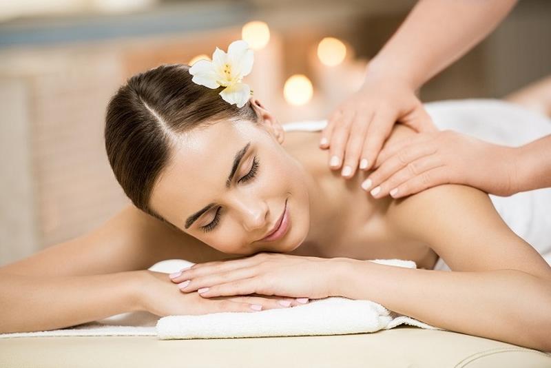 Người mẹ sau sinh đang nằm thư giãn trên giường massage chuyên nghiệp, chuyên viên nữ massage nhẹ nhàng vùng bụng và hông