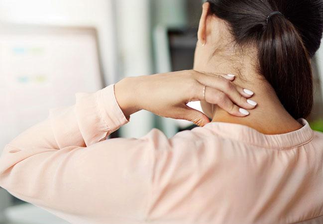 Một phụ nữ đang mệt mỏi xoa bóp vai gáy sau khi trở về từ chuyến du lịch, hành lý để ở phía sau