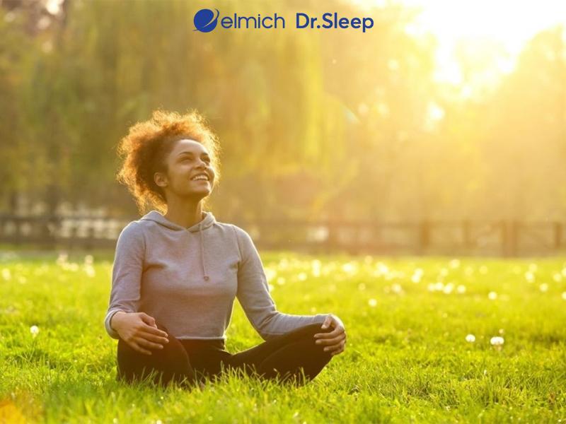 Phụ nữ trung niên đang thư giãn trong phòng tắm nắng ấm áp, tay đặt nhẹ nhàng lên bụng dưới, biểu cảm bình an và tự tin sau quá trình chăm sóc vùng kín