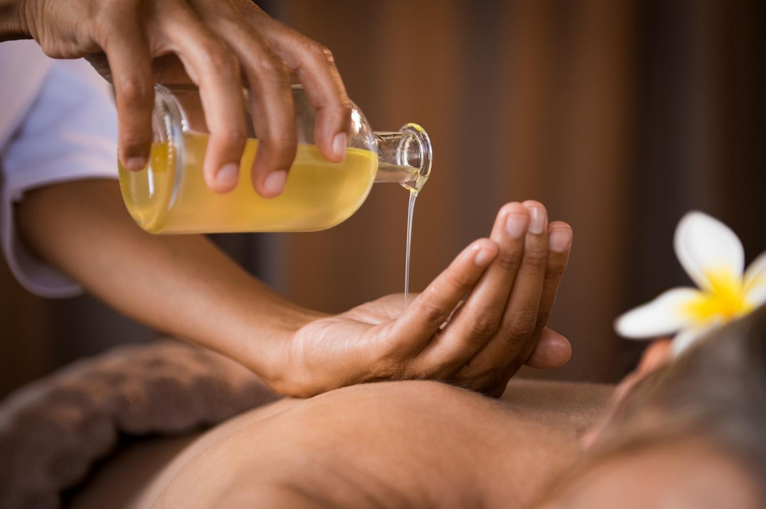 Bàn tay therapist thực hiện thao tác massage tinh dầu trên lưng khách hàng với kỹ thuật khai mở luân xa