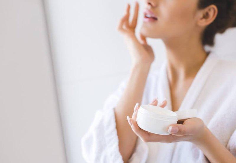 Một phụ nữ đang nhẹ nhàng thoa kem dưỡng ẩm chuyên dụng lên mu bàn tay, tượng trưng cho việc chăm sóc vùng kín bị khô rát